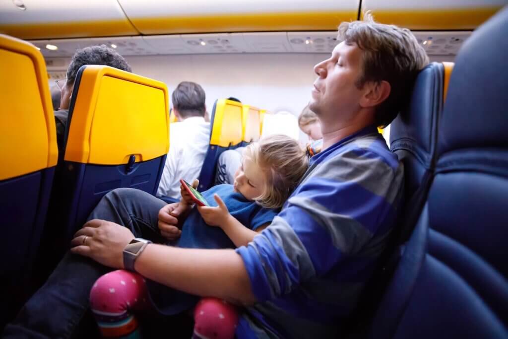Image of Young father holding his baby toddler daughter during flight on airplane going on vacations. Tired man and cute girl during night flight. child playing with smartphone. Family sitting in plane.