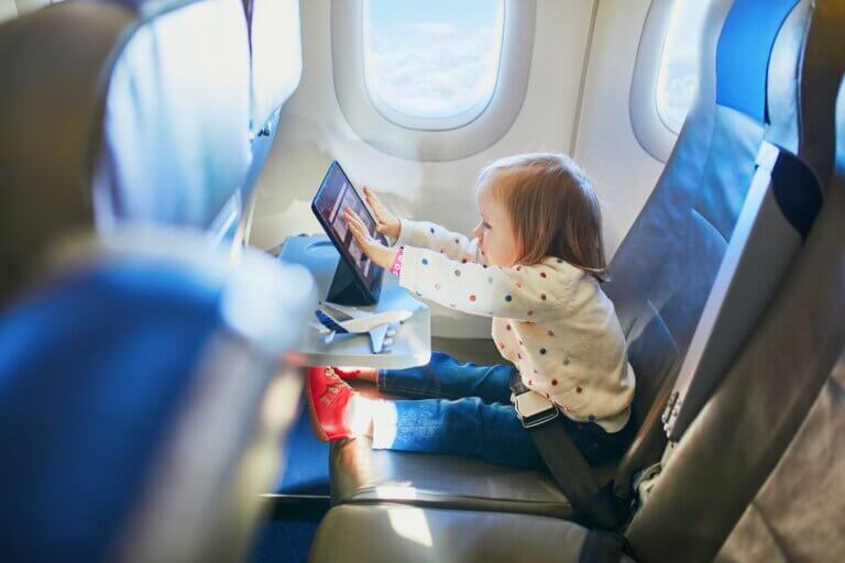 Check out the top tips for flying with a toddler recommended by top family travel blog Marcie in Mommyland. Image of a Adorable little toddler girl traveling by plane. Small child sitting by aircraft window and using a digital tablet during the flight. Traveling abroad with kids. Unaccompanied minor concept