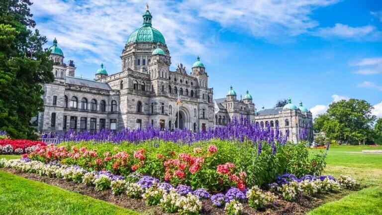 Check out these tips for planning a romantic weekend getaway to downtown Victoria BC by top Seattle blog Marcie in Mommyland. Image of Beautiful view of historic parliament building in the citycenter of Victoria with colorful flowers on a sunny day, Vancouver Island, British Columbia, Canada
