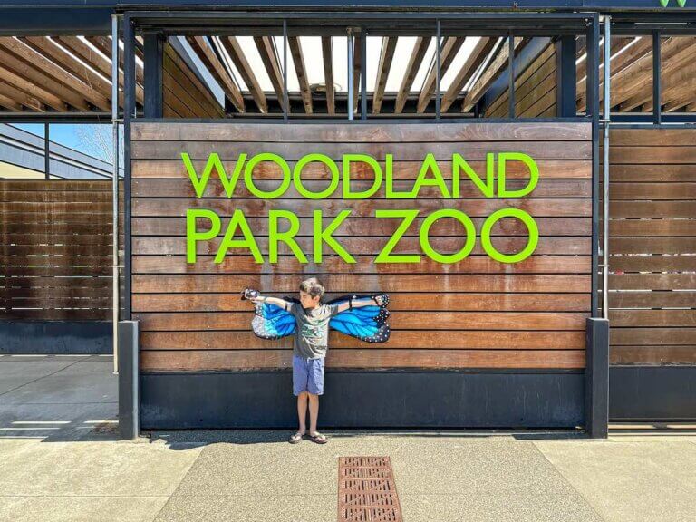 Check out this guide to Woodland Park Zoo by top Seattle blogger Marcie in Mommyland. Image of a boy wearing blue butterfly wings in front of the Woodland Park Zoo sign