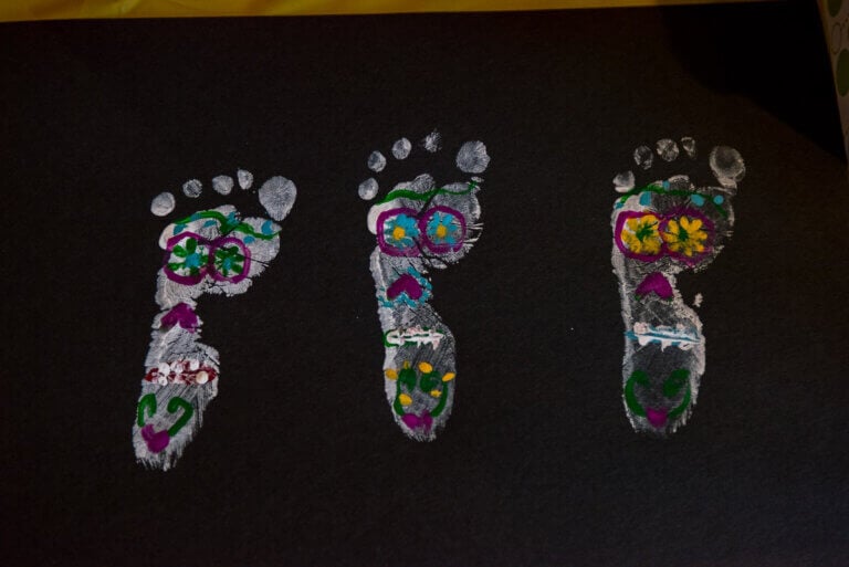 Check out this Dia de los Muertos baby feet painting activity by top family travel blog Marcie in Mommyland. Image of baby footprints with sugar skulls painted on them