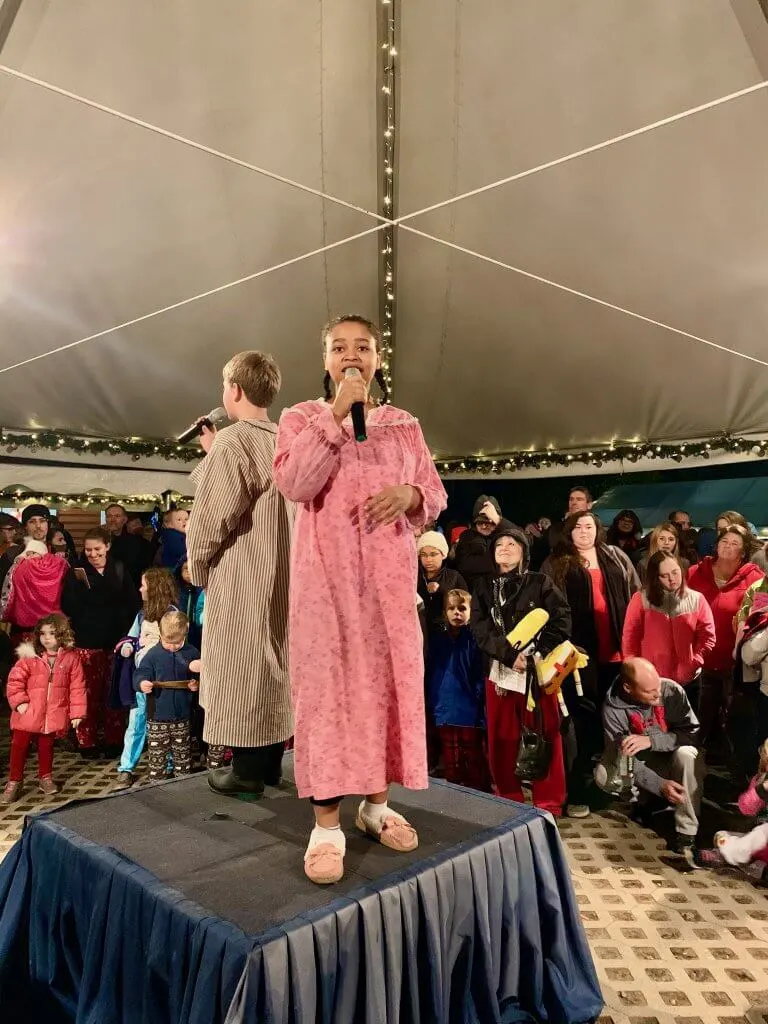 All Aboard the Polar Express™ Train Ride at Mt Rainier Railroad and Logging Museum review featured by top Seattle blogger, Marcie in Mommyland: Photo of a girl dressed in a pink nightgown and a boy wearing a brown robe singing "Believe" in a Christmas-themed outdoor tent