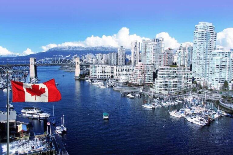 Check out this amazing 4-day Vancouver itinerary with kids by top Seattle blog Marcie in Mommyland. Image of Canadian flag in front of view of False Creek and the Burrard street bridge in Vancouver, Canada.