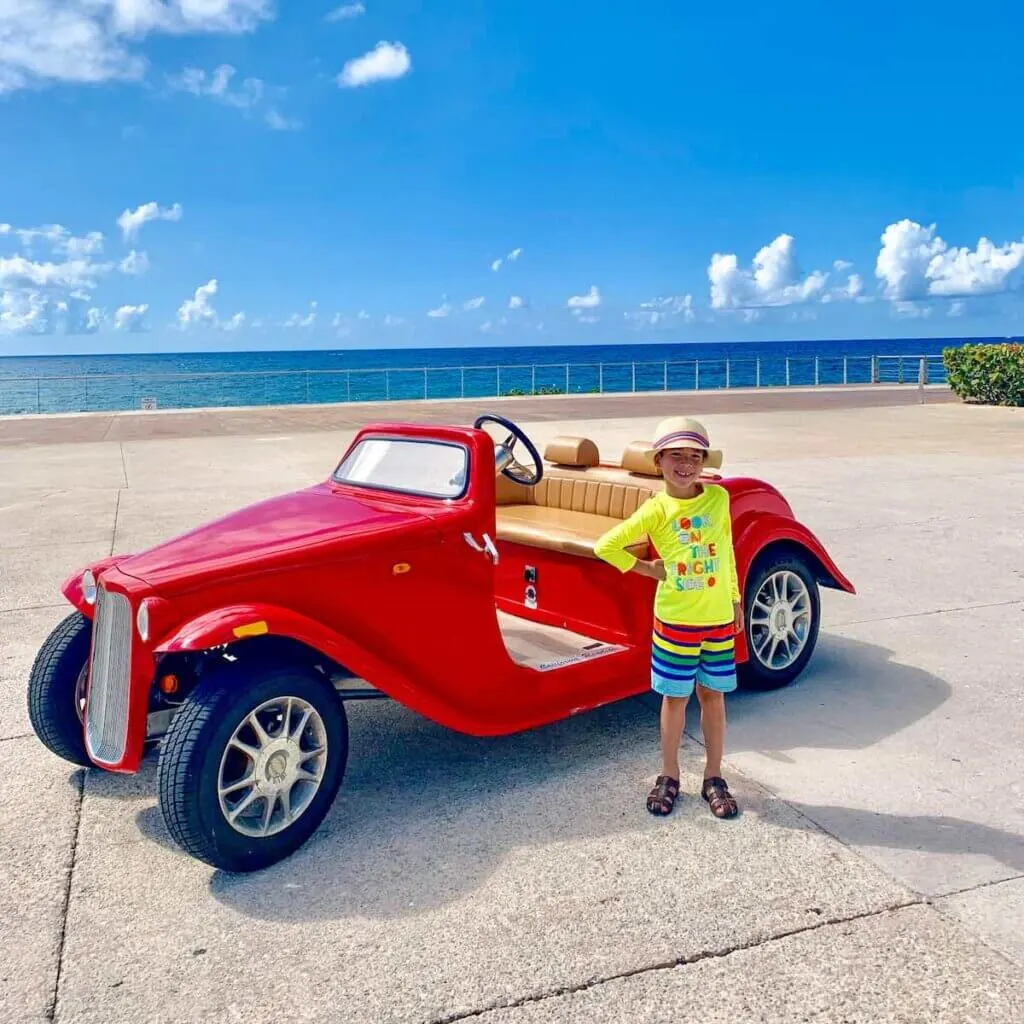 Image of a boy standing in front of a vintage red car at the Hard Rock Riviera Maya resort