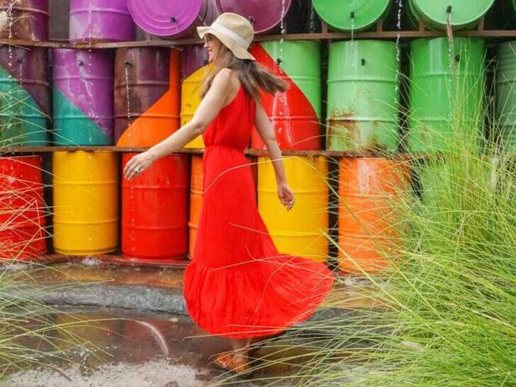 Check out the coolest things to do in Costa Mesa California recommended by top family travel blog Marcie in Mommyland. Image of a woman wearing a red dress twirling in front of colorful rain barrels