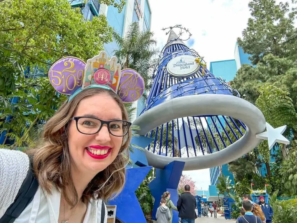 Check out the top ten reasons to stay at the Disneyland Hotel in Anaheim by top family travel blog Marcie in Mommyland. Image of a woman wearing Minnie ears taking a selfie outside of the Disneyland Hotel
