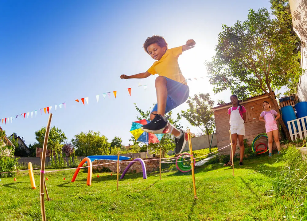 The Ultimate List of Indoor Games, Activities and Workouts to Keep Your Kids Active featured by top Seattle lifestyle blogger, Marcie in Mommyland: Cute black curly hair boy jump over strings passing course of obstacles playing competitive game with friends