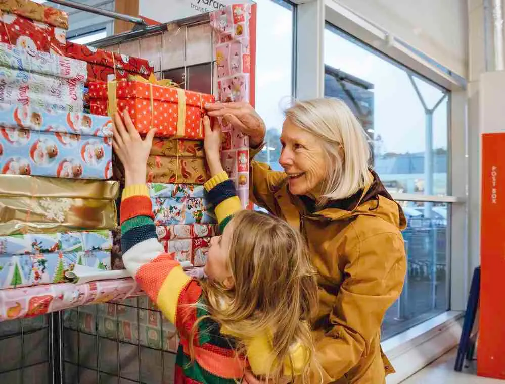 Volunteering is a great family Christmas tradition. Image of Little girl and her grandmother are donating a Christmas charity box in their local supermarket.