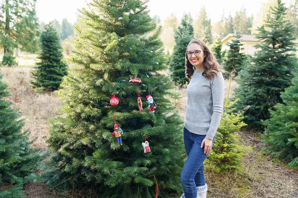 How to take your own DIY Christmas Family Portraits, tips featured by top Seattle lifestyle blogger, Marcie in Mommyland. Christmas tree farms are the ultimate spot for outdoor Christmas pictures. Image of a mom posing in front of a tree at a Christmas tree farm.