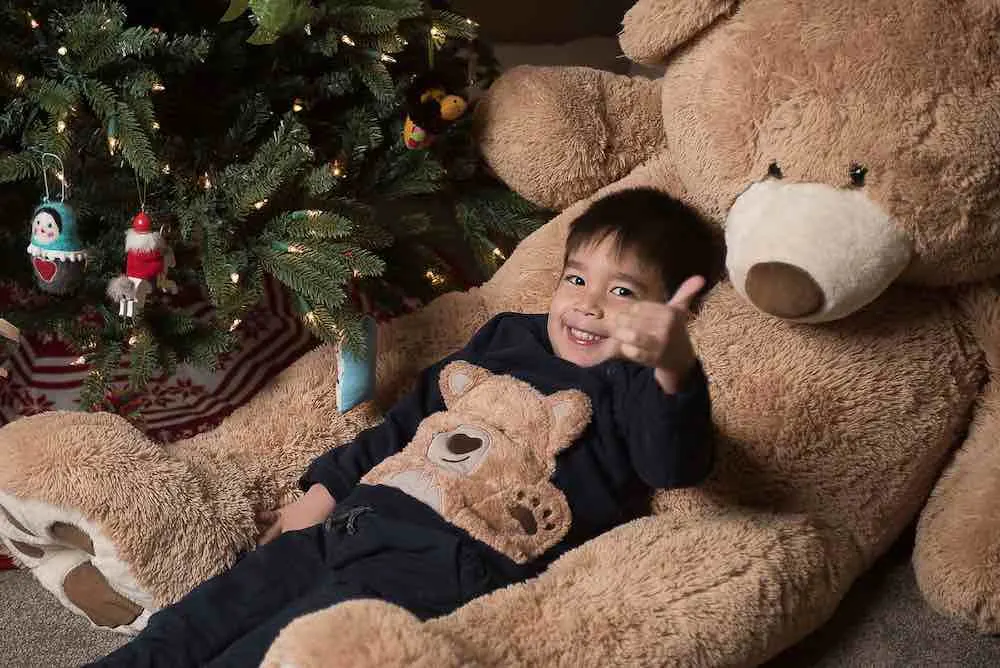 How to take your own DIY Christmas Family Portraits, tips featured by top Seattle lifestyle blogger, Marcie in Mommyland. Consider taking Christmas family portraits in front of your Christmas tree. Image of a boy lounging in a giant teddy bear in front of a Christmas tree.