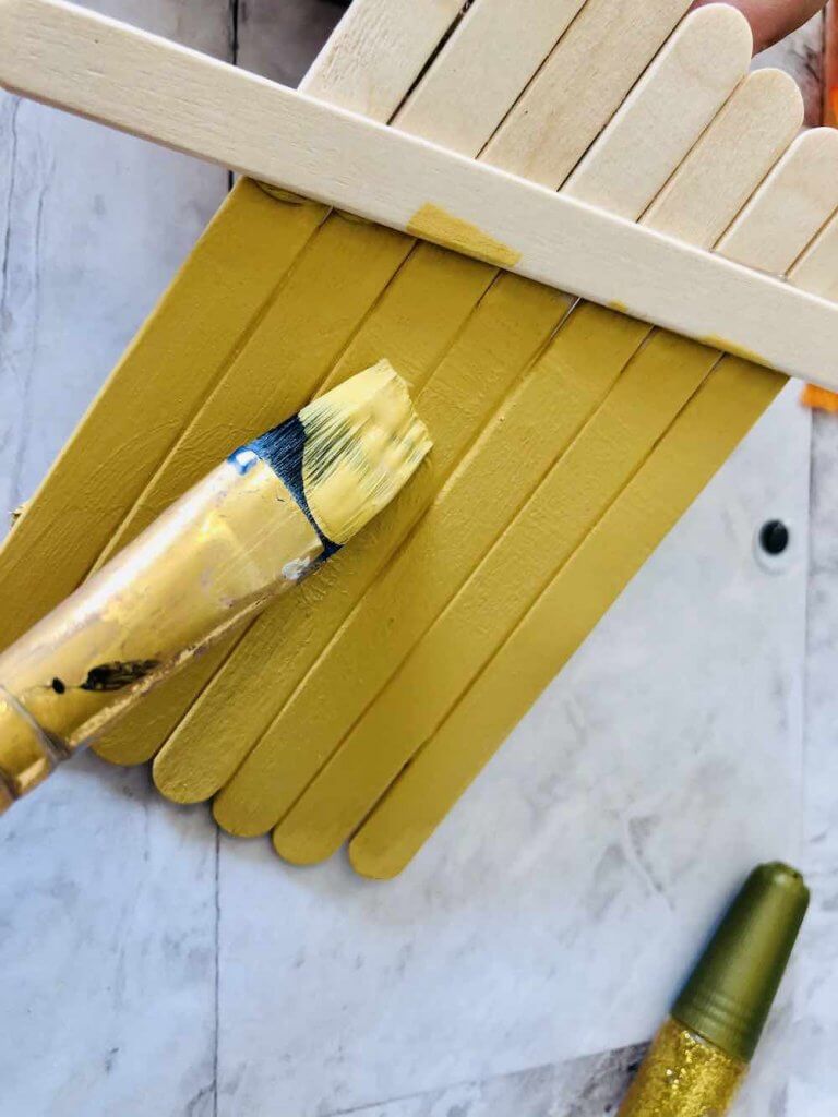 How to make a popsicle stick scarecrow craft step 4. Image of someone painting popsicle sticks yellow