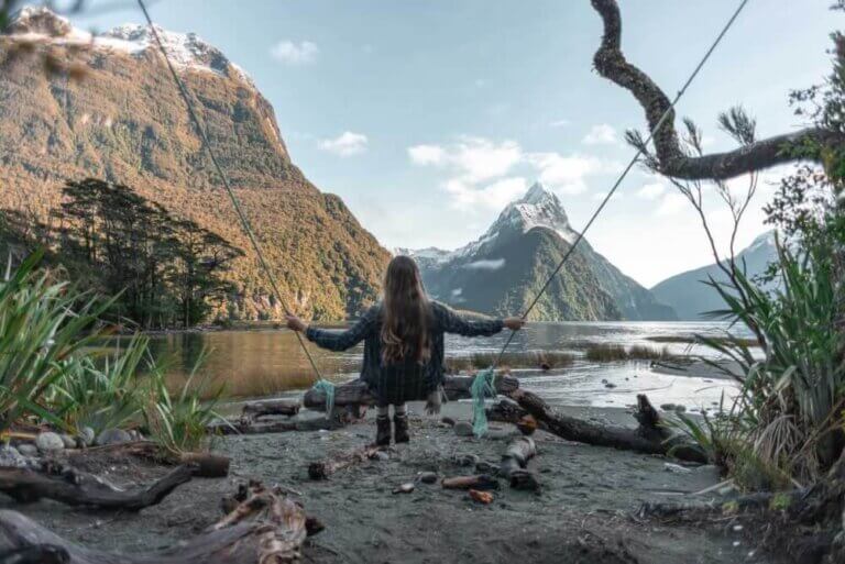 Find out the best things to do in NZ South Island. Image of a woman sitting on a swing outside at a New Zealand beach.
