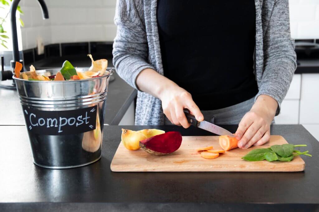 Image of a woman chopping vegetables and putting the scraps in a compost pail