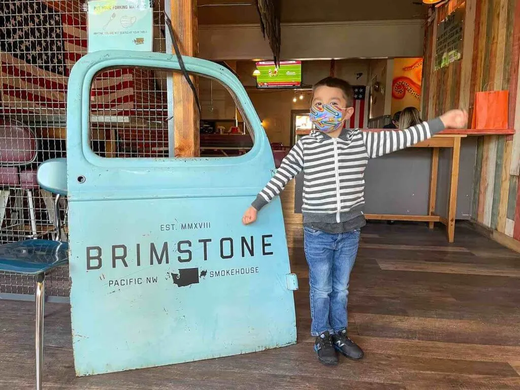Brimstone PNW Smokehouse is one of the top Gig Harbor restaurants for families. Image of a boy posing next to a truck door with the name of the Gig Harbor restaurant on it.