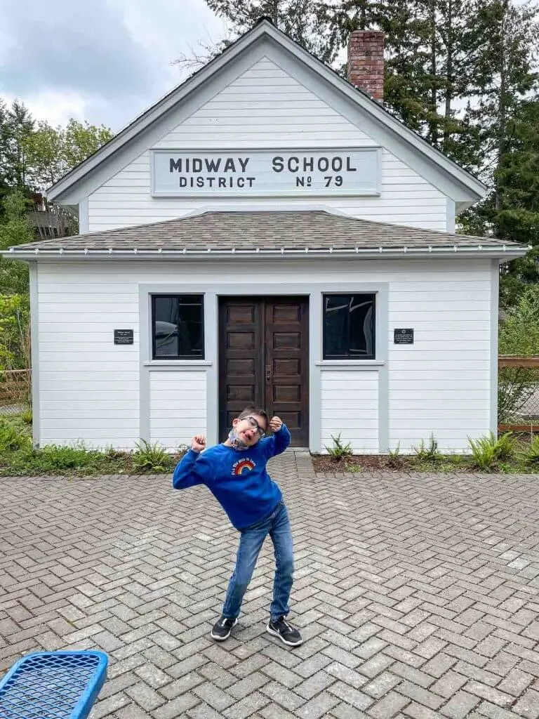 Visiting the Harbor History Museum is a top thing to do in Gig Harbor Washington. Image of a boy doing a funny pose outside of a one room school house.