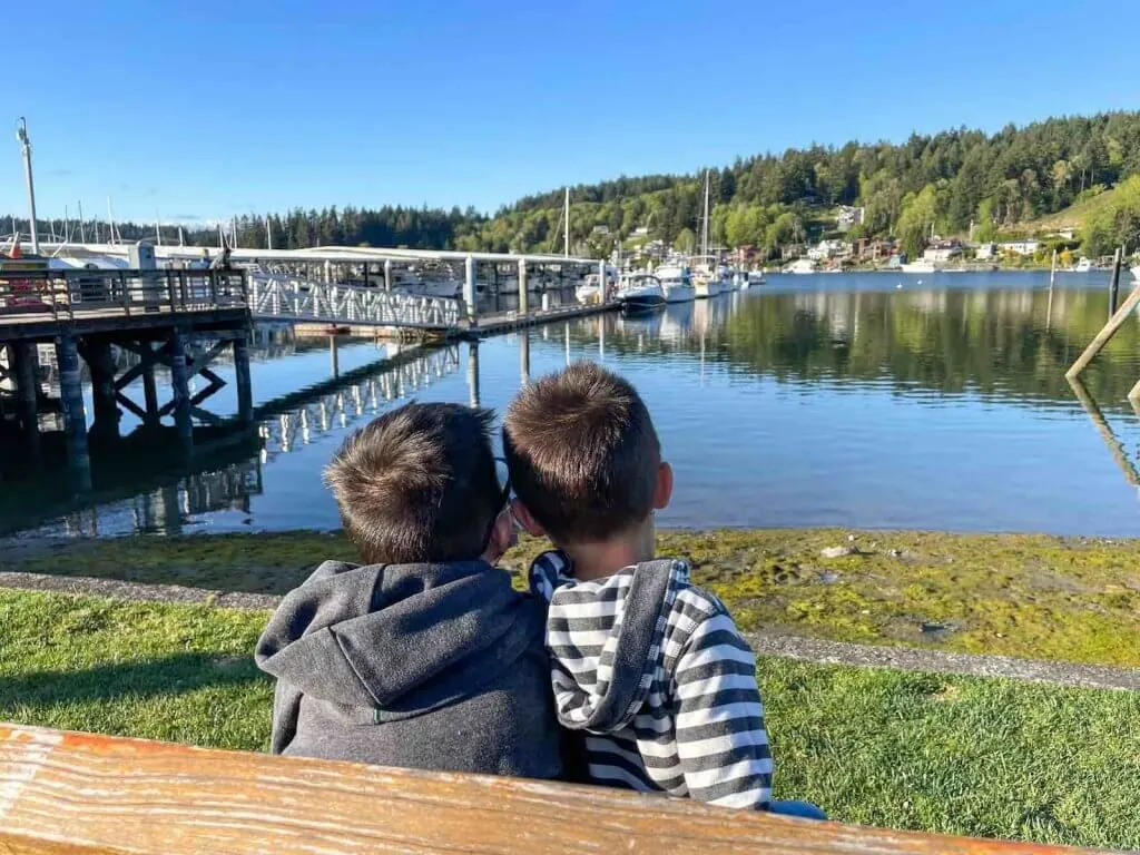 You'll definitely want to check out Skansie Park while you walk along the Gig Harbor waterfront. Image of two boys sitting on a bench looking at the waterfront in Gig Harbor, which is one of the best Weekend Getaways in Washington.