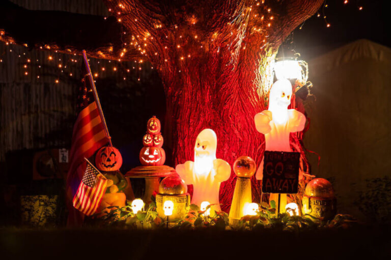Find out the best Halloween lights to get for a spooky yard this Halloween season. Image of pumpkins, a lit up ghost and orange lights on a tree.