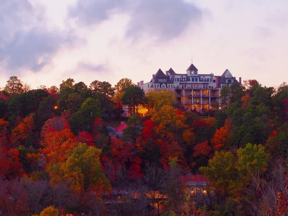 The Crescent Hotel is one of the spookiest Halloween hotels in the United States. Image of a grand hotel sitting on a hill surrounded by trees in fall.