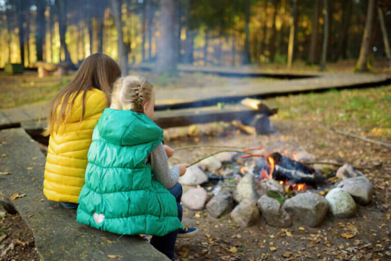 Get my top tips for camping in the fall with kids plus my fall camping packing list for families. Image of two girls roasting marshmallows by the fire.