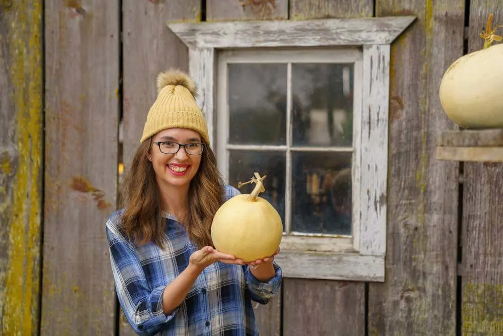 Gordon Skagit Farms is one of the best Washington State pumpkin patches for photos. Image of a woman holding a white pumpkin in front of a barn window.
