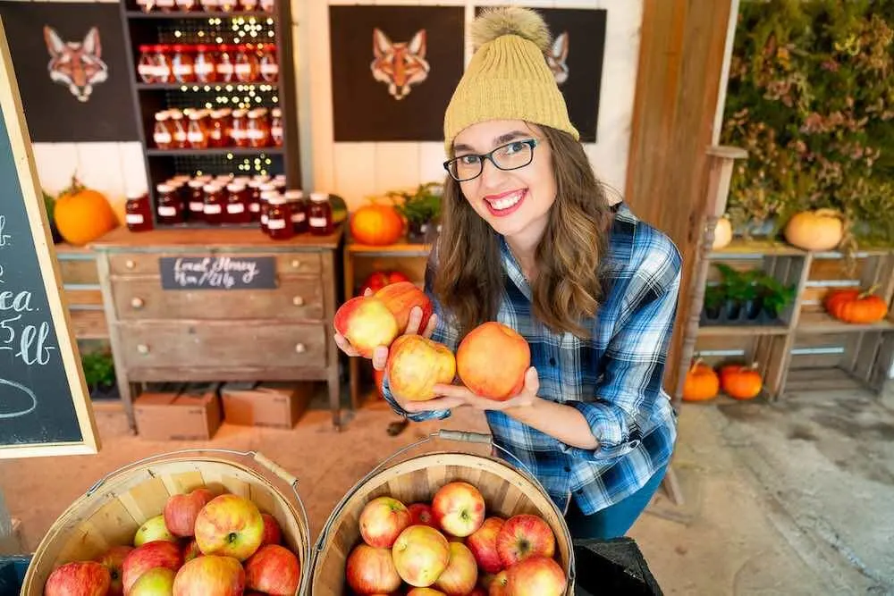 You can find fresh produce at Gordon Skagit Farms, a pumpkin patch near Seattle, WA. Image of a woman holding red apples inside a barn.