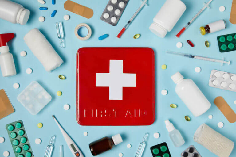 Find out what to pack in a family travel first aid kit for kids by top family travel blog Marcie in Mommyland. Image of a red first aid kit surrounded by medical supplies.