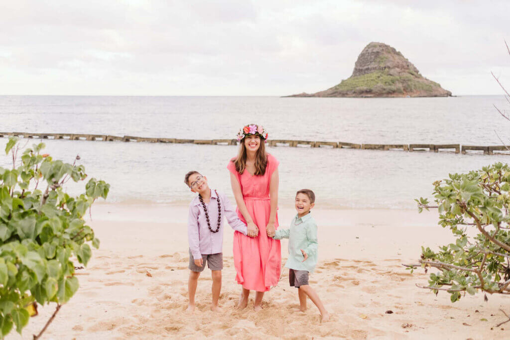 Find out the best Hawaiian island for kids recommended by a mom who's visited Hawaii more than 35 times! Image of a mom and two boys holding hands at Kualoa Beach Park on Oahu.