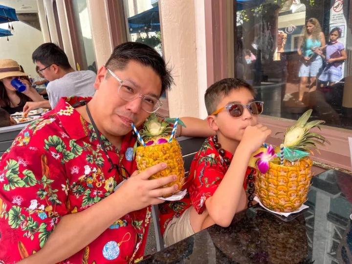 Find out the best things to do on Oahu with kids by top Seattle blog Marcie in Mommyland. Image of a dad and son wearing red Aloha shirts and sipping pineapple drinks.