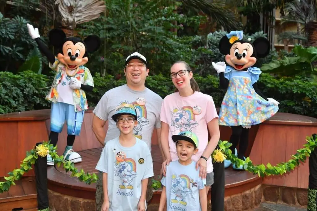 Photo of a family of four posing with Mickey and Minnie Mouse wearing Hawaiian print clothing.