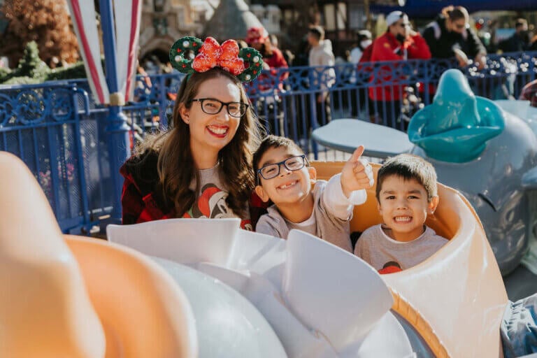 Disneyland vs LEGOLAND California: Which is right for your family? Image of a mom and two boys in the Dumbo ride at Disneyland.