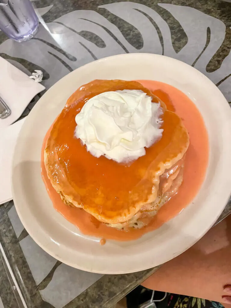 One of the best things to do on Oahu with kids is get pancakes at Cinnamon's. Image of a plate of guava chiffon pancakes topped with whipped cream.
