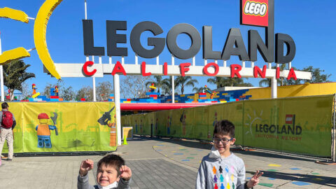 Find out the best tips for LEGOLAND California by top family travel blog Marcie in Mommyland. Image of two boys standing in front of the LEGOLAND California entrance.