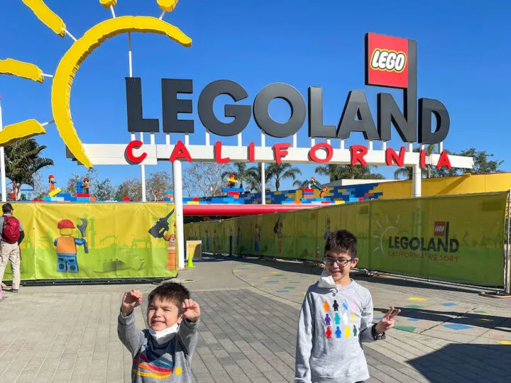 Find out the best tips for LEGOLAND California by top family travel blog Marcie in Mommyland. Image of two boys standing in front of the LEGOLAND California entrance.