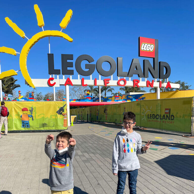 Find out the best tips for LEGOLAND California by top family travel blog Marcie in Mommyland. Image of two boys standing in front of the LEGOLAND California entrance.