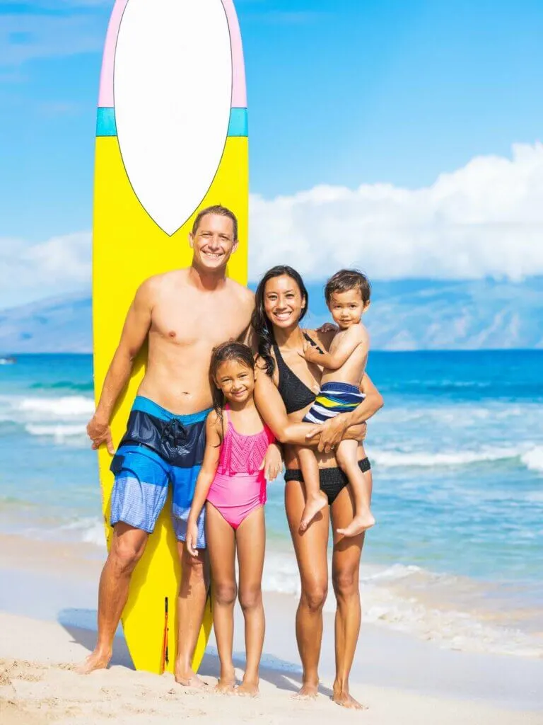 Image of a family posing on a beach with a surfboard.