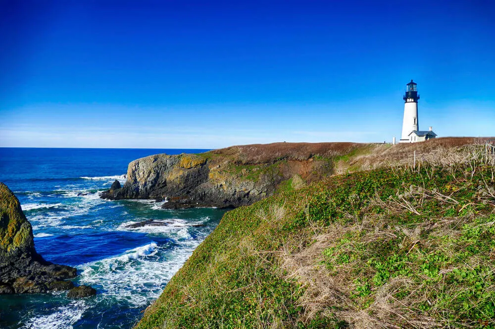 Image of a white lighthouse on a rocky bluff overlooking the ocean at Newport, and Oregon Coastal town.