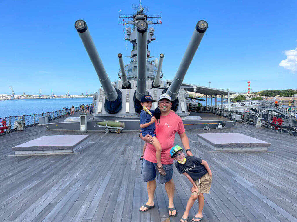 Image of a dad with two boys posing on the deck of the USS Battleship Missouri at Pearl Harbor on Oahu.