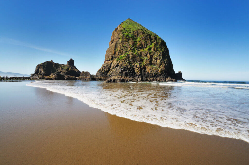Image of Haystack Rock on a golden sandy beach on the Oregon Coast town of Cannon Beach.