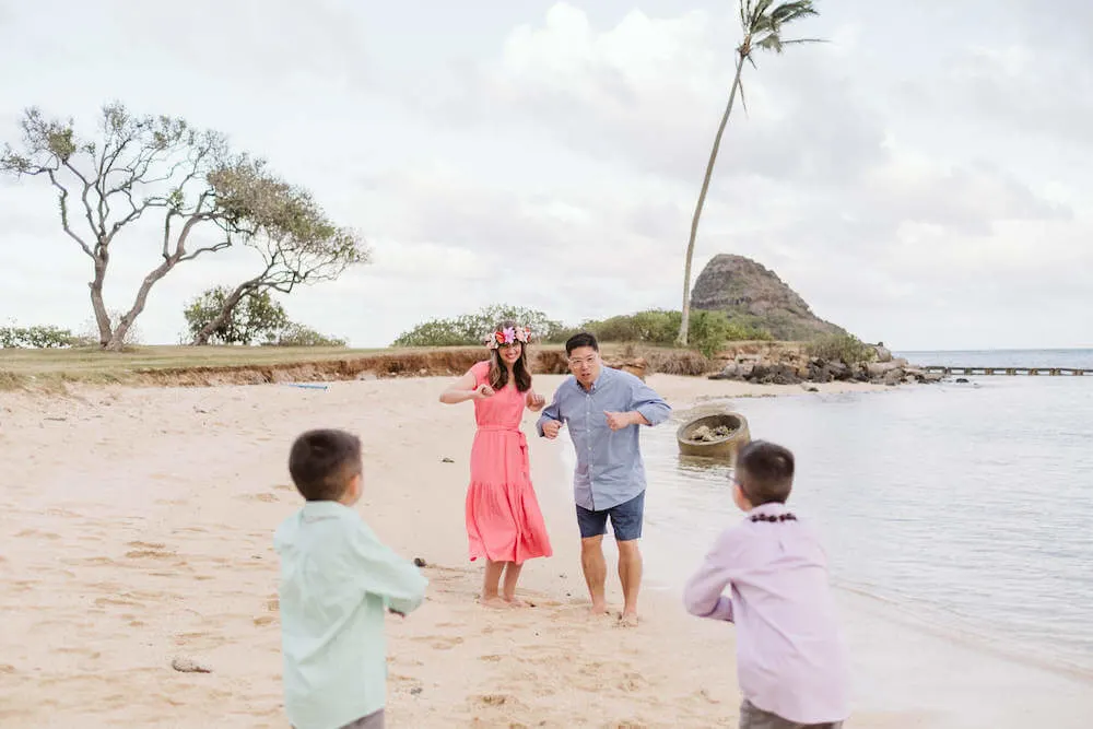 Image of a mom and dad dancing on the beach with two boys trying to make them laugh.