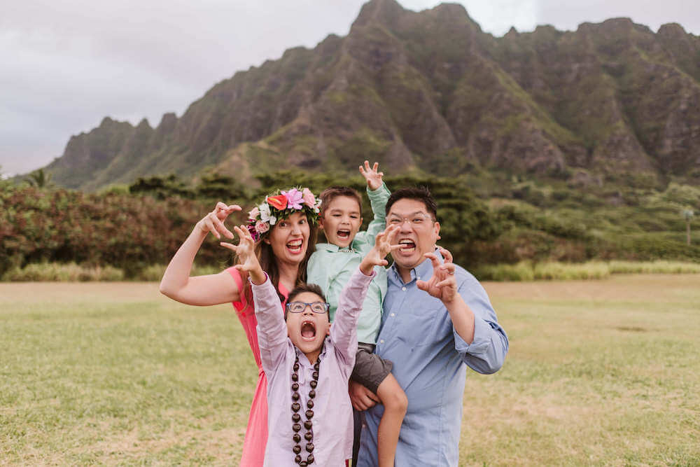 Image of a family dressed in pastel colors pretending to be dinosaurs with Kualoa mountains in the background.