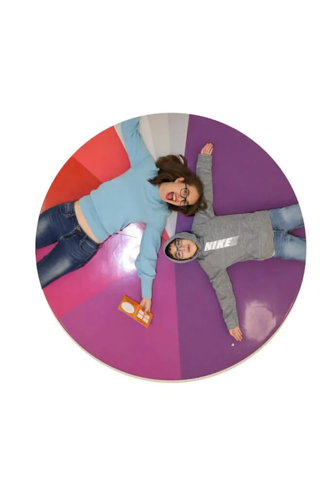 Round image of a mom and boy laying on a colorful ottoman at the Color Factory in NYC