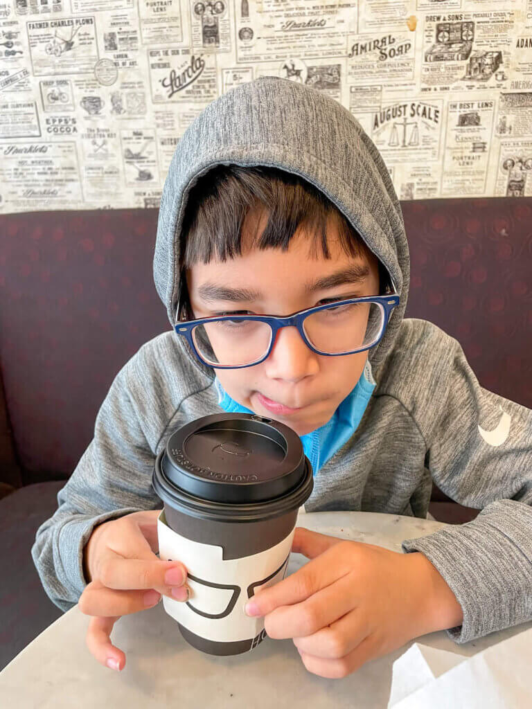 Image of a boy wearing a hoodie and glasses with a coffee cup