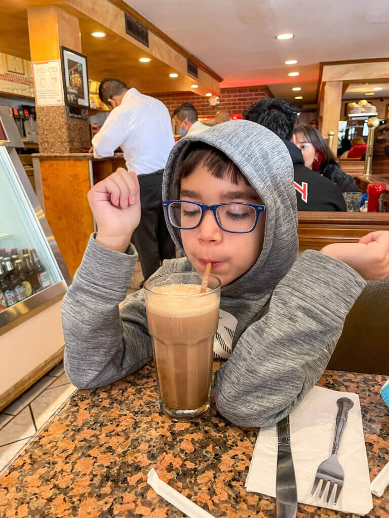 Image of a boy sipping on a chocolate egg cream drink at a diner in NYC
