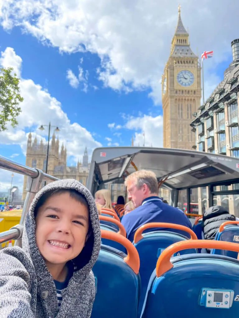 Image of a boy in a hooded sweater sitting on the upper deck of a double decker bus with Big Ben in the background