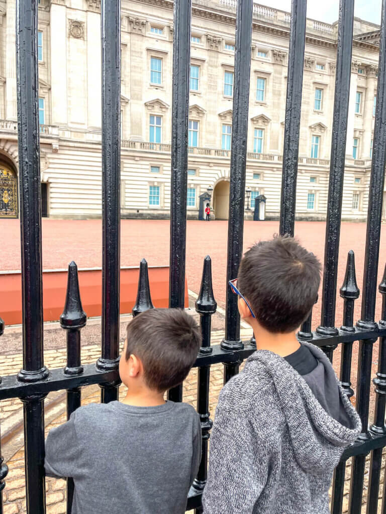 Image of two boys looking through the gate at Buckingham Palace to see the guards