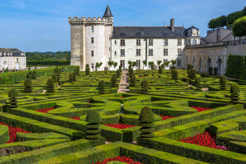 Image of a white chateau with a gorgeous garden with green hedges and pink flowers in the Loire Valley in France