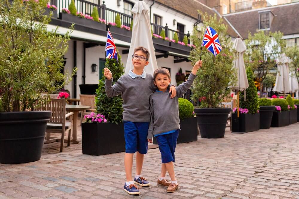 Image of two boys wearing grey sweaters and blue shorts waving British flags at a London photo shoot