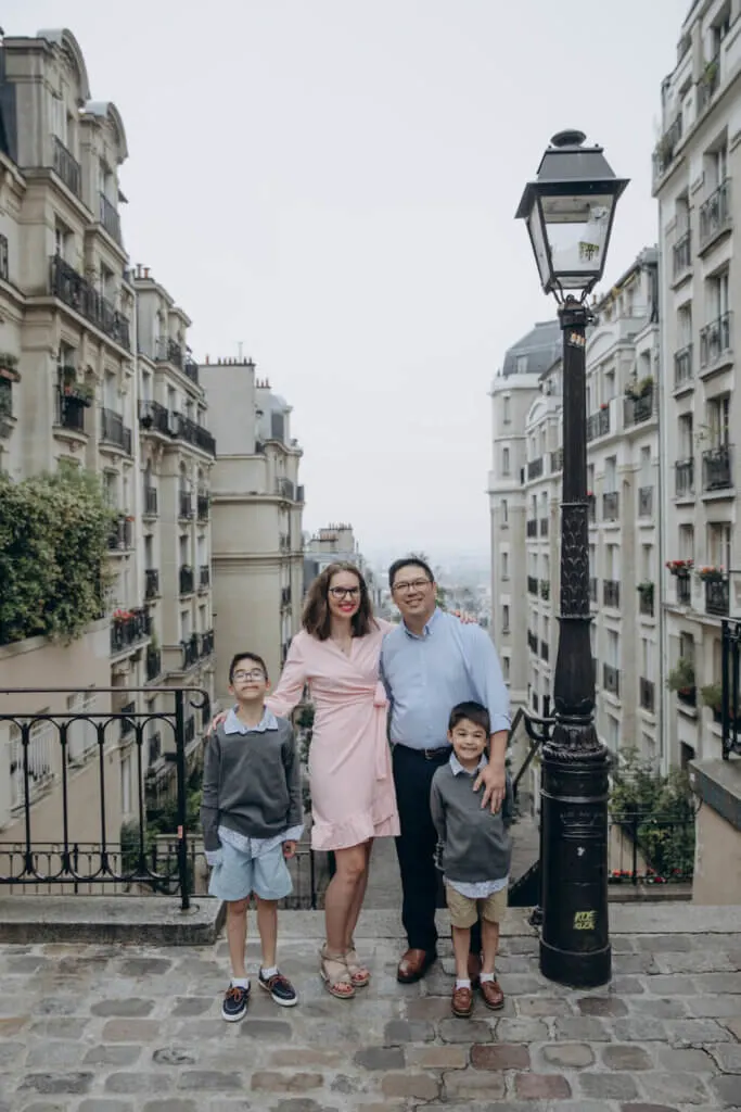 Image of a mom wearing pink and dad and two boys wearing blue and grey clothing posing on a street in Montmartre Paris.