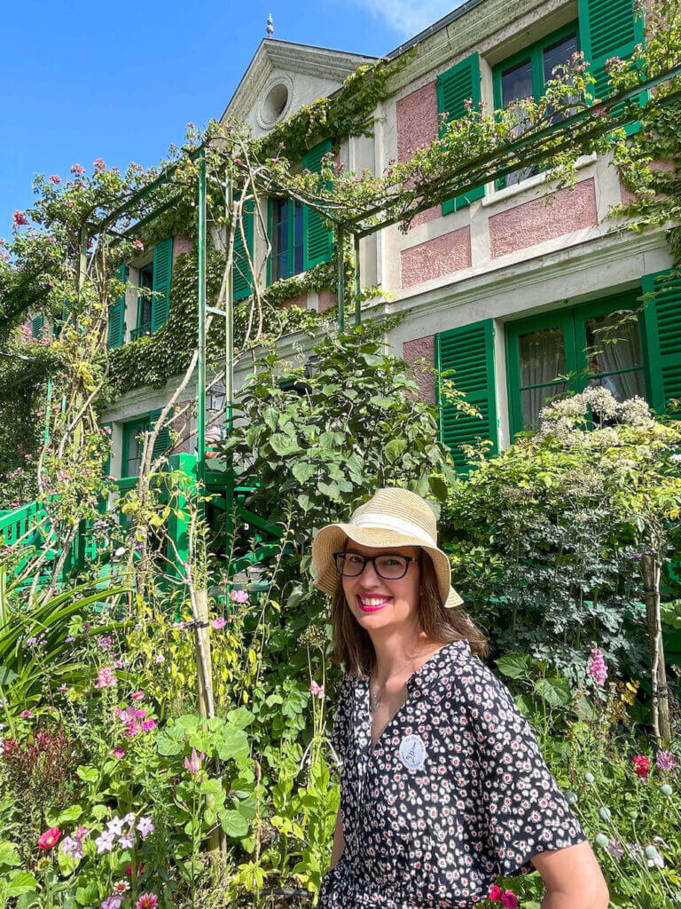 Image of a woman standing in front of a pink and green house in Giverny Franch