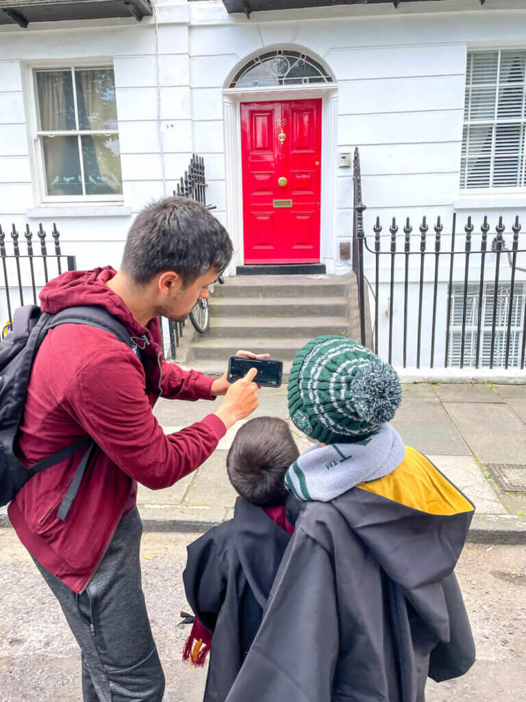 Image of a man showing two boys a video on his phone in front of a red door in London where they filmed Harry Potter